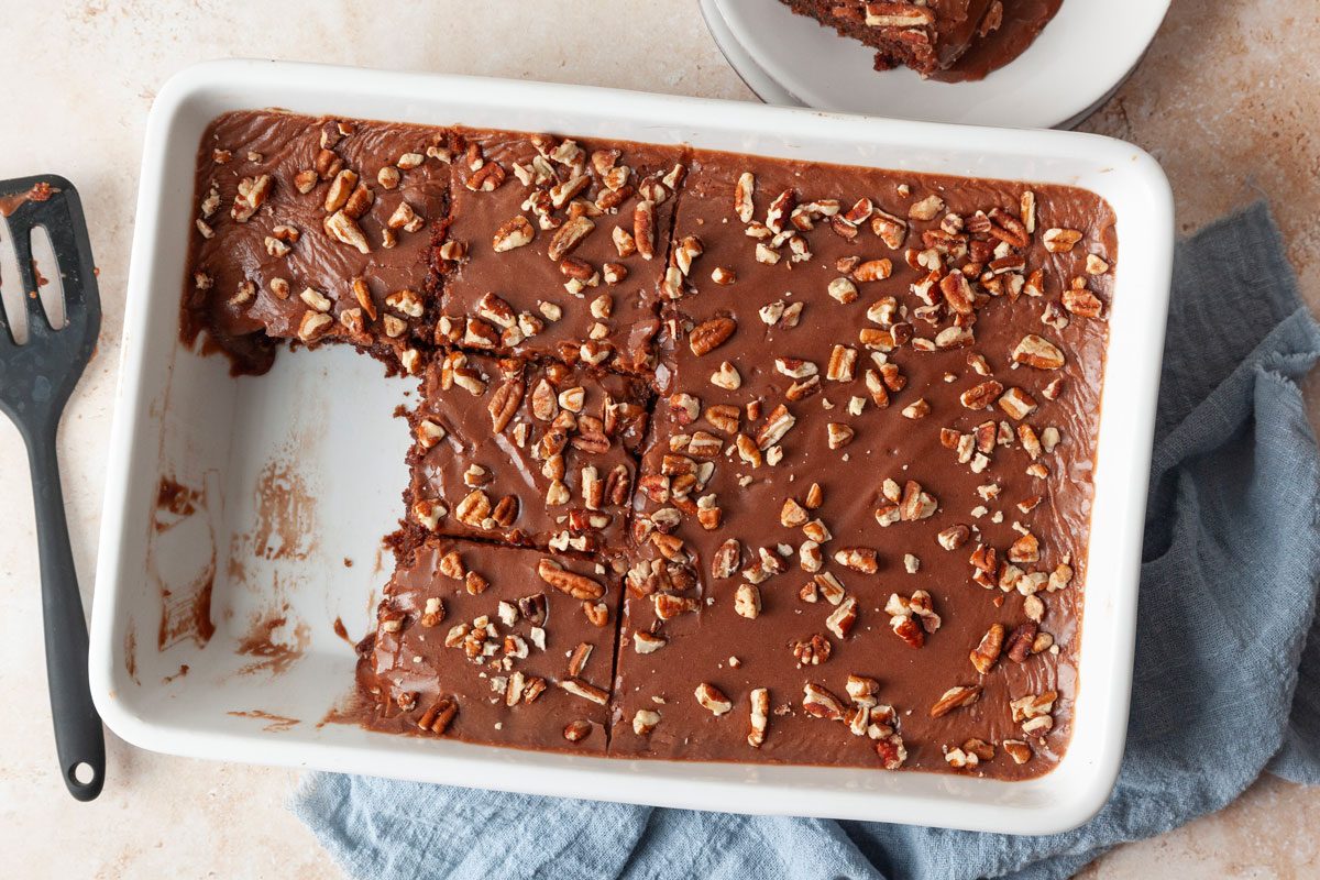Full yield of Taste of Home Buttermilk Chocolate Cake in a white 13x9 baking dish, a few pieces out