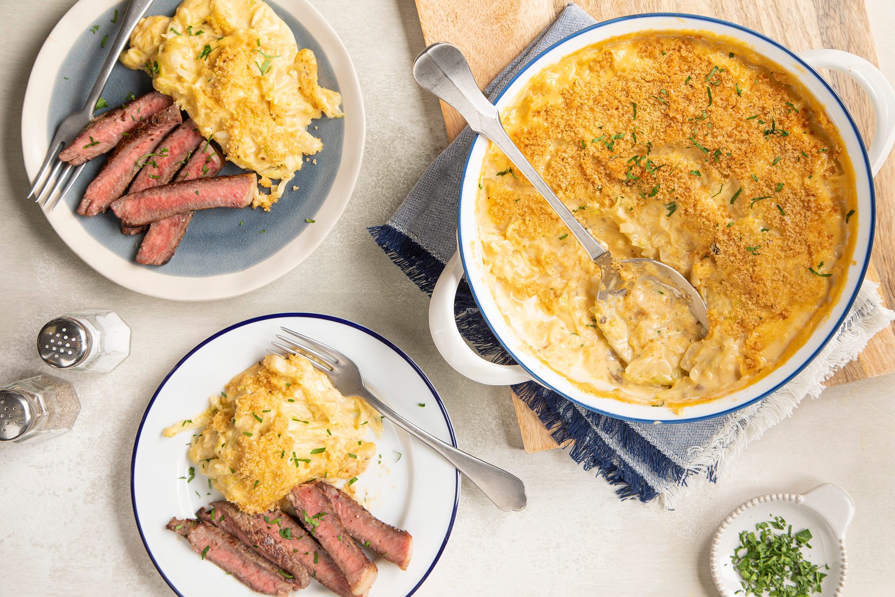 A baking dish filled with baked macaroni and cheese topped with a crispy, golden breadcrumb crust. The dish is set on a light-colored wooden surface, and there is a small bowl containing additional breadcrumbs next to it.