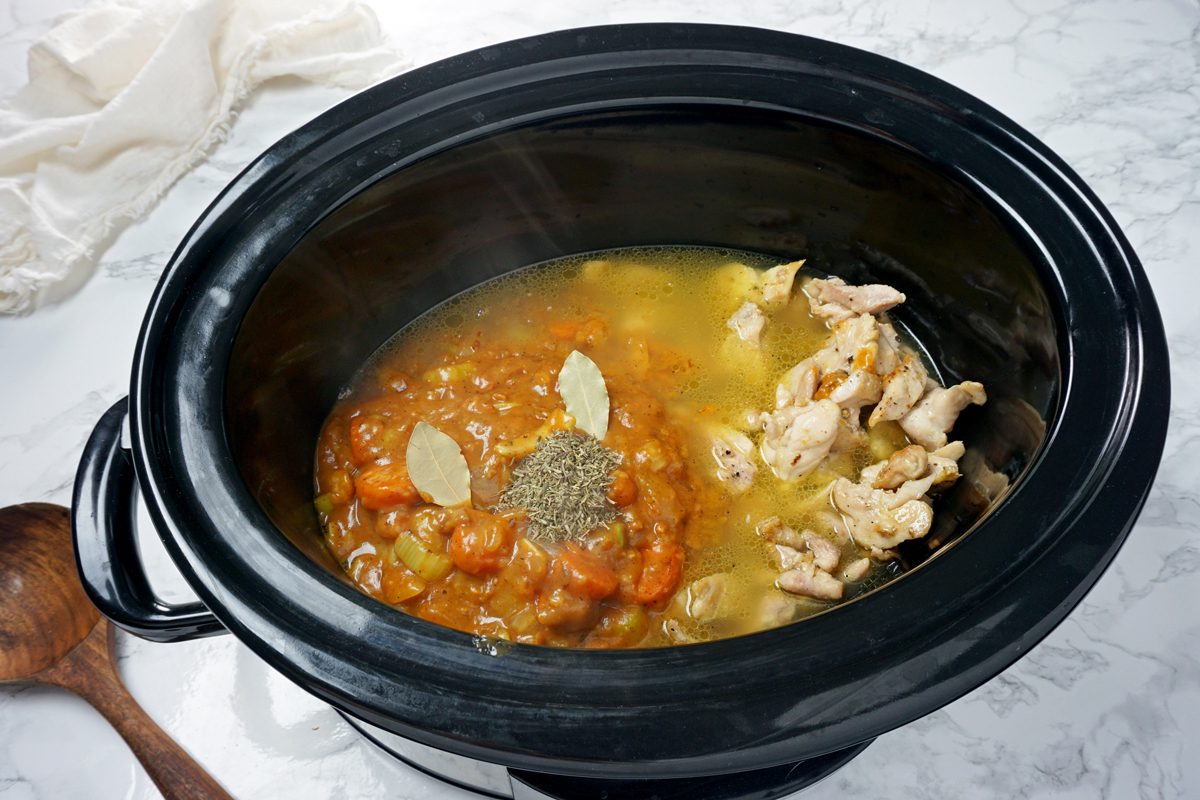 A slow cooker with broth, chicken, herbs, and vegetables to make Crock-Pot Chicken and Dumplings RMS 201122 for Taste of Home