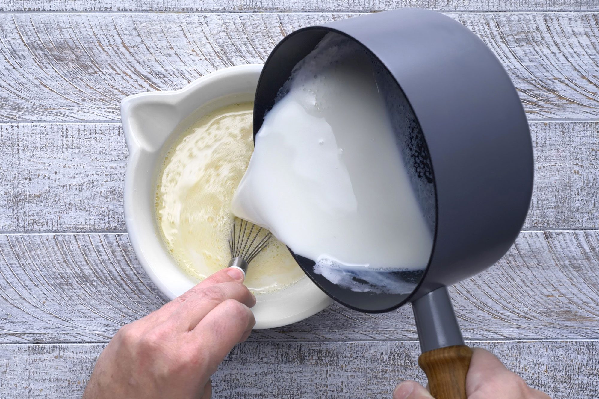 Overhead shot of a small saucepan; heat milk until bubbles form around sides of pan; remove from heat slowly stir in hot milk; stir in vanilla; wooden background;