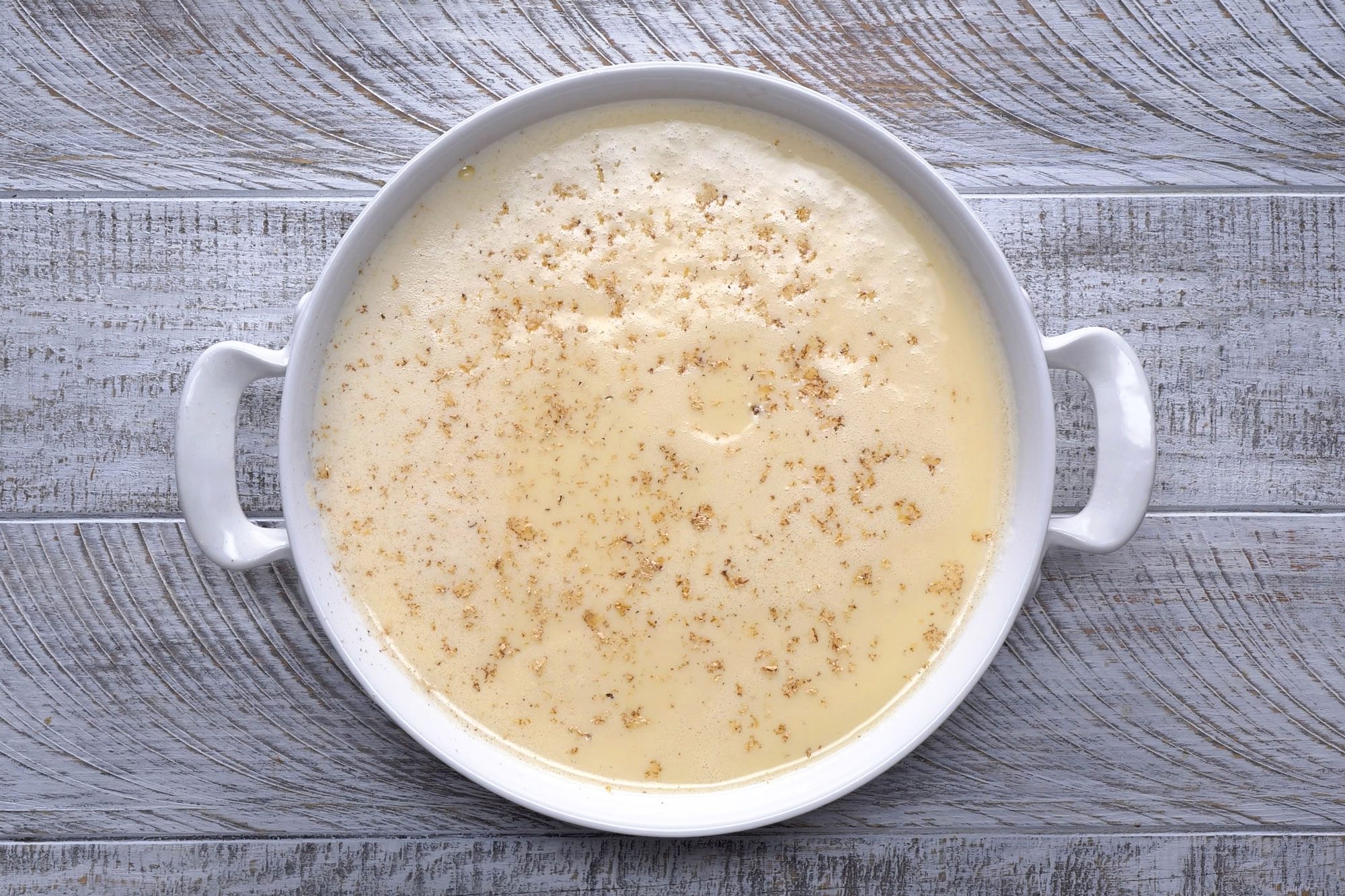 Overhead shot of remove baking dish from water bath immediately to a wire rack; cool 30 minutes; refrigerate until cold; sprinkle with nutmeg; wooden background;