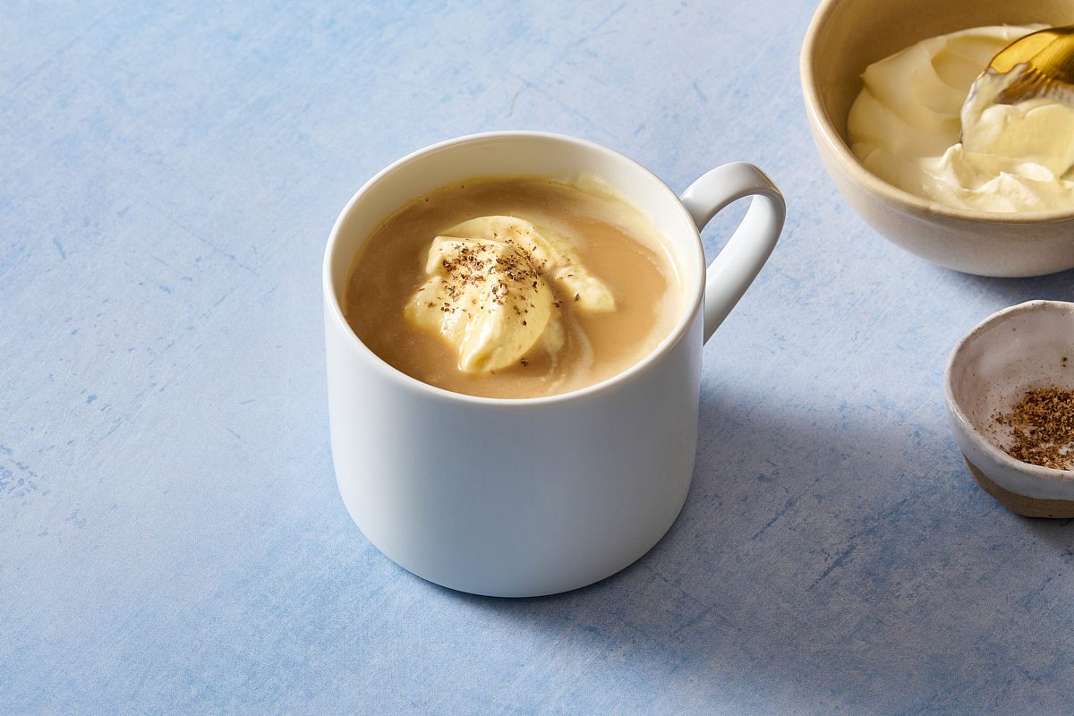 A mug of eggnog coffee with whipped cream and grated nutmeg in the background