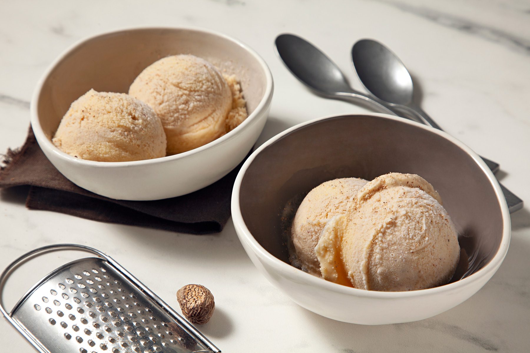 Eggnog Ice Cream in two bowls with nutmeg, grater and spoons