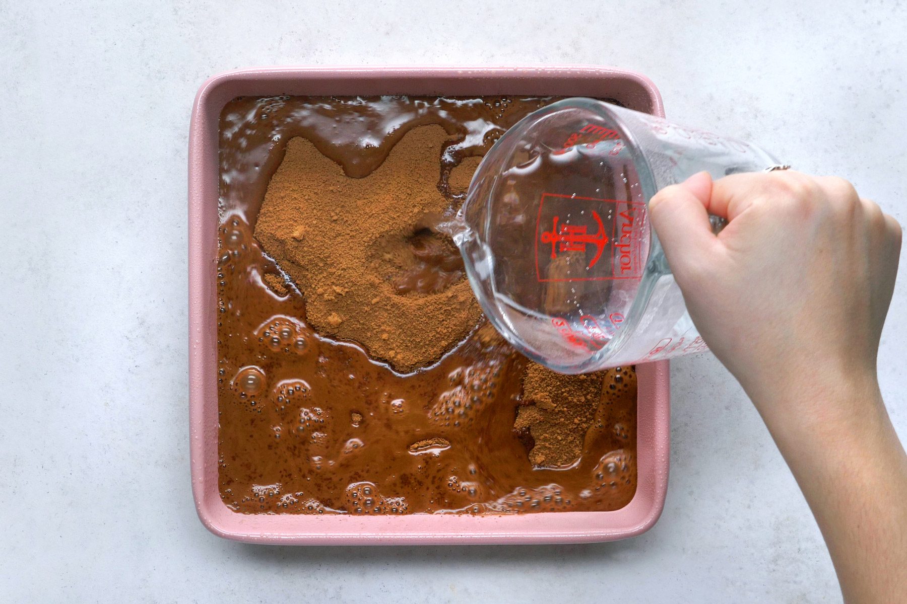Hot water is being poured over the fudge batter in a square pan.
