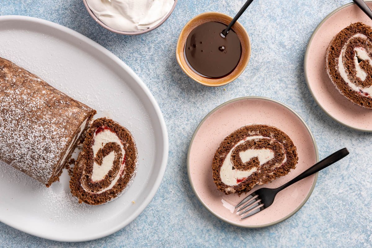 Taste of Home Ice Cream Cake Roll recipe photo the cake rolled up sprinkled with powdered sugar and sides of chocolate sauce and whipped cream.