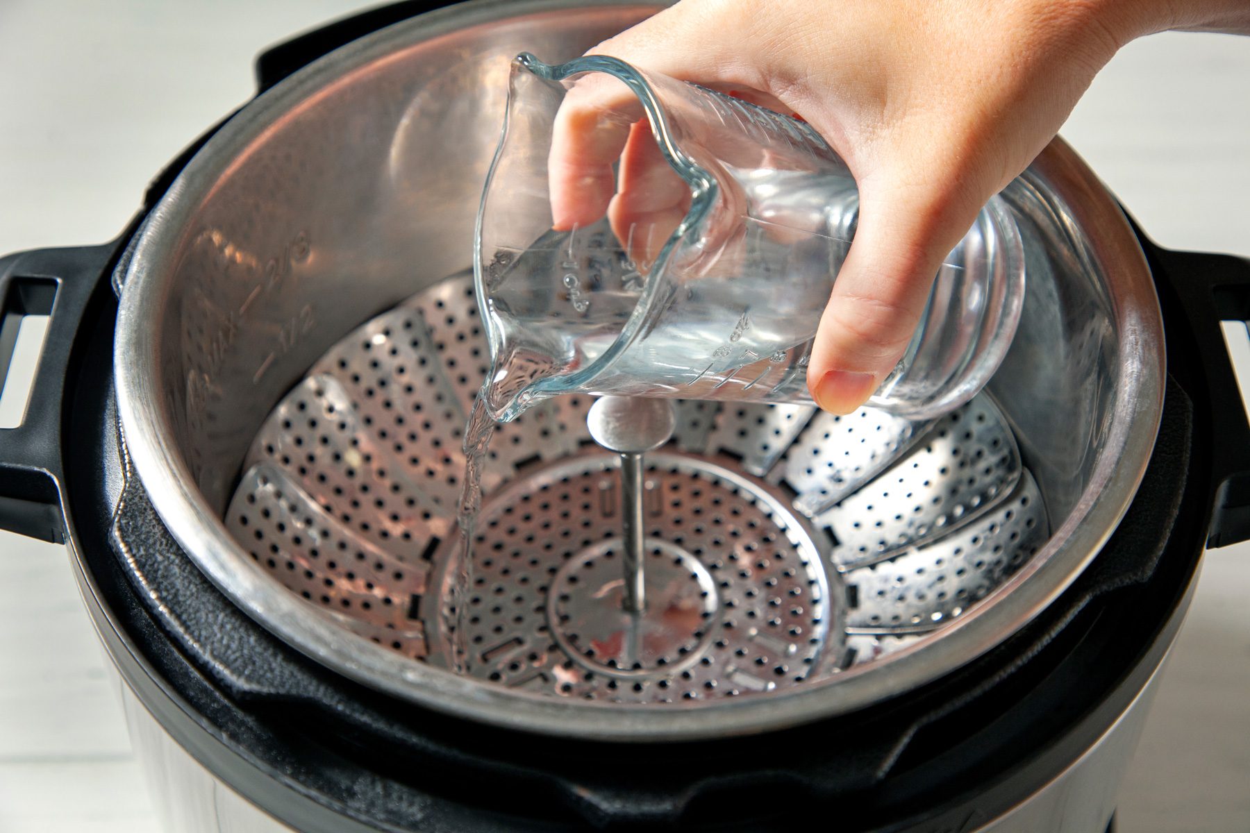 Hand pouring water in a steamer basket inside instant pot