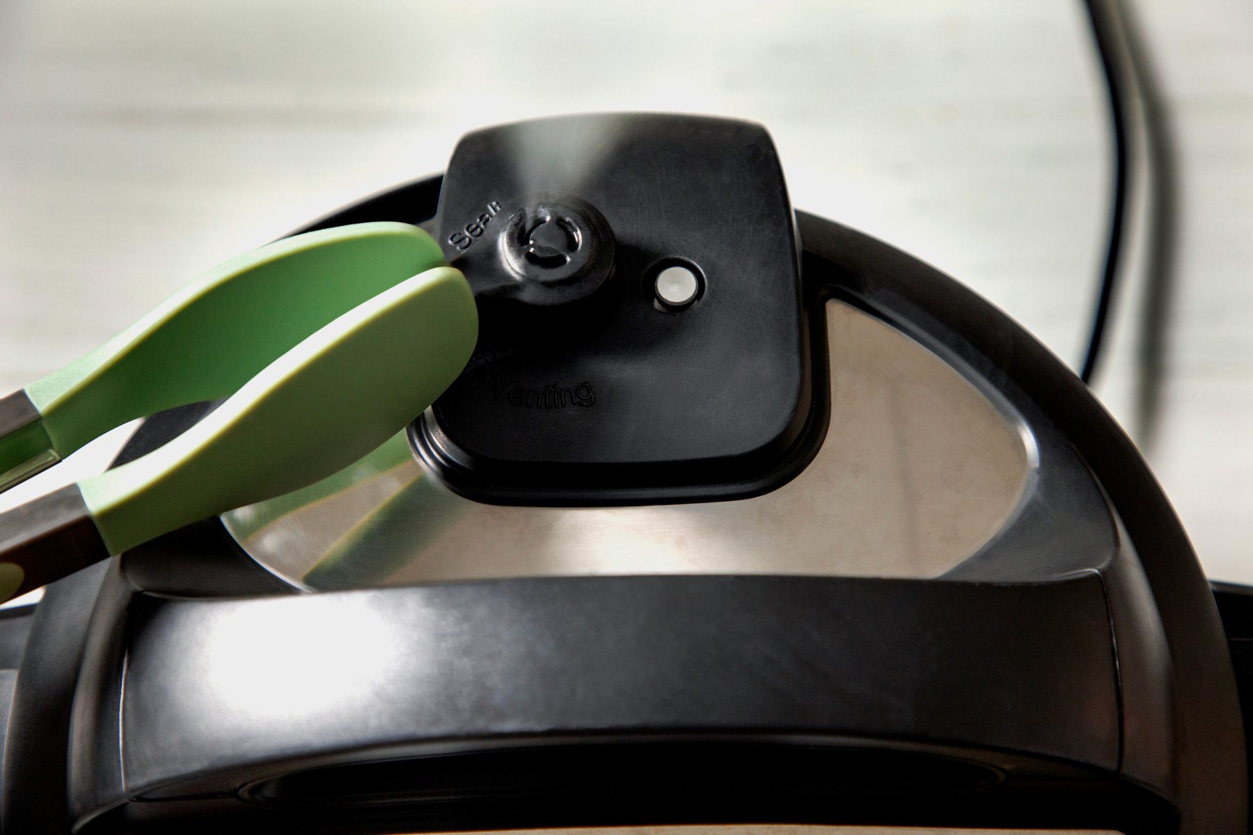 Pressing quick release on Instant Pot with tongs to release pressure