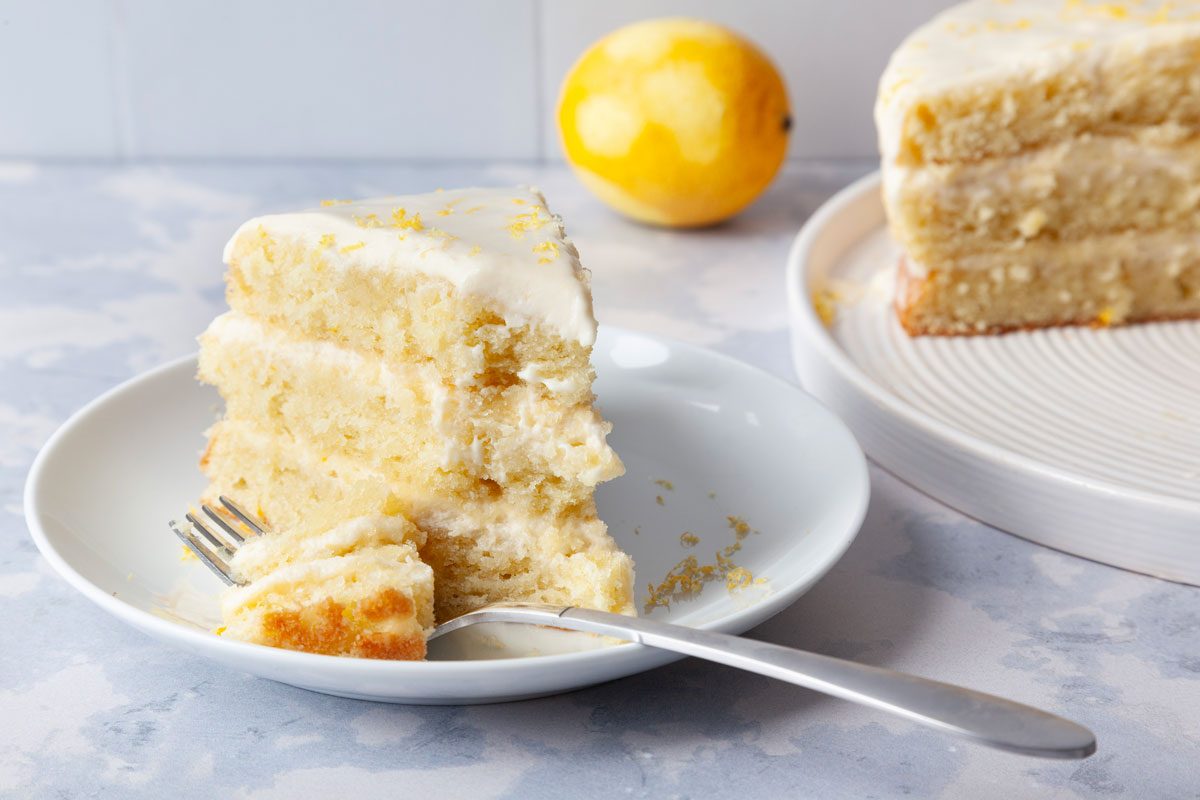 Single serving of Taste of Home Italian Lemon Cream Cake on awhite pate, garnished with lemon zest, full yield and zested lemon peaking in