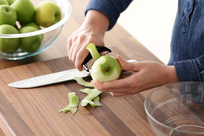 Person peeling a green apple