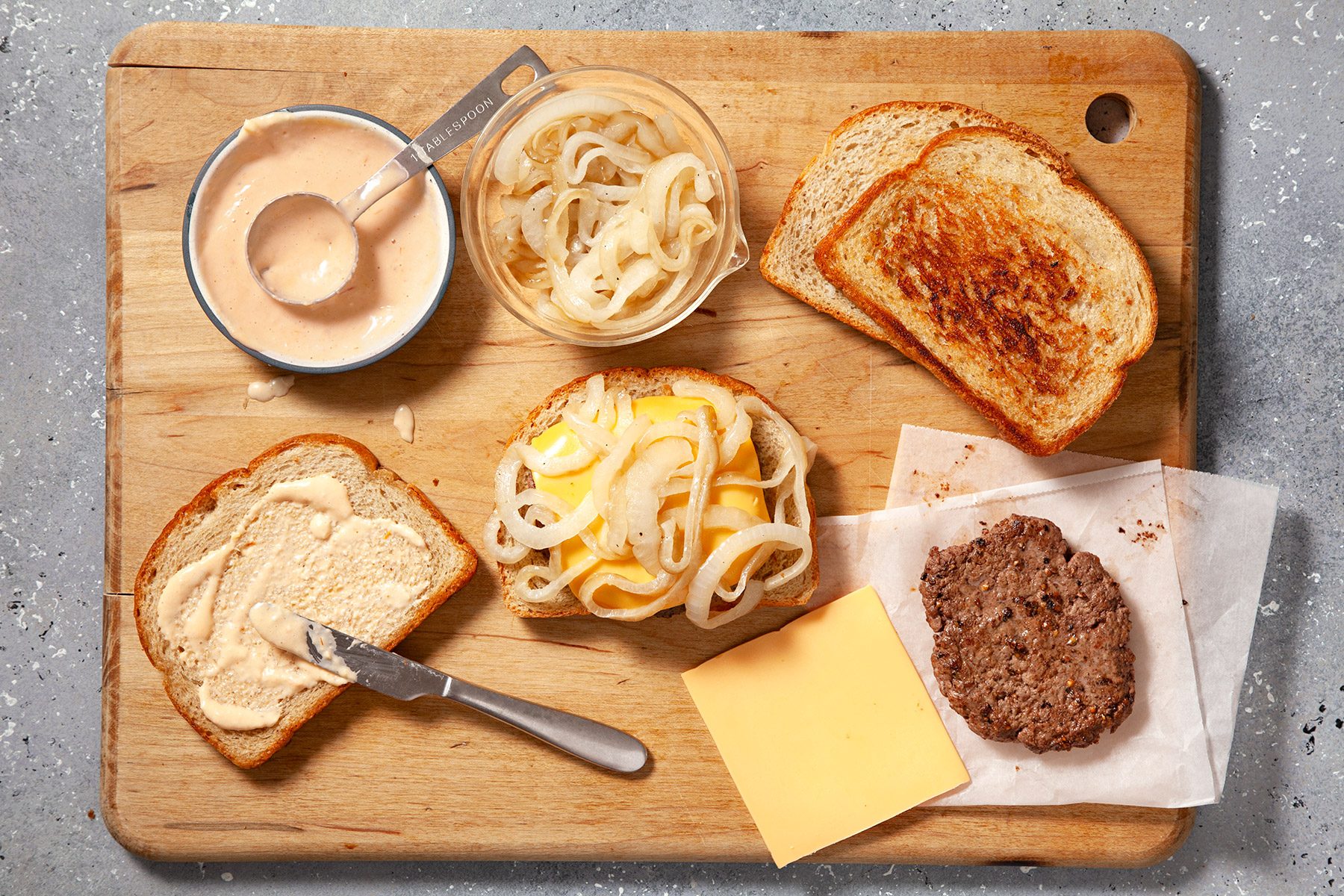 overhead shot; grey tetxured background; Patty Melts ingredients placed over wooden board;