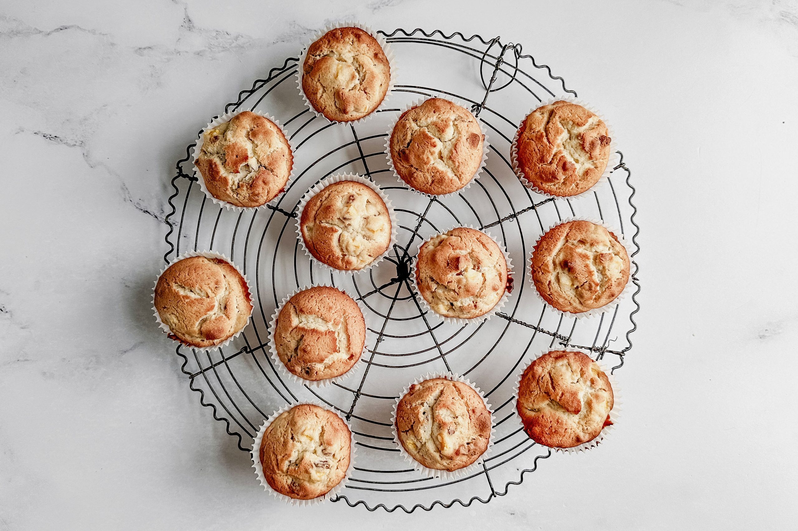 Taste of Home peach muffins on a round wire cooling rack on a marble surface.