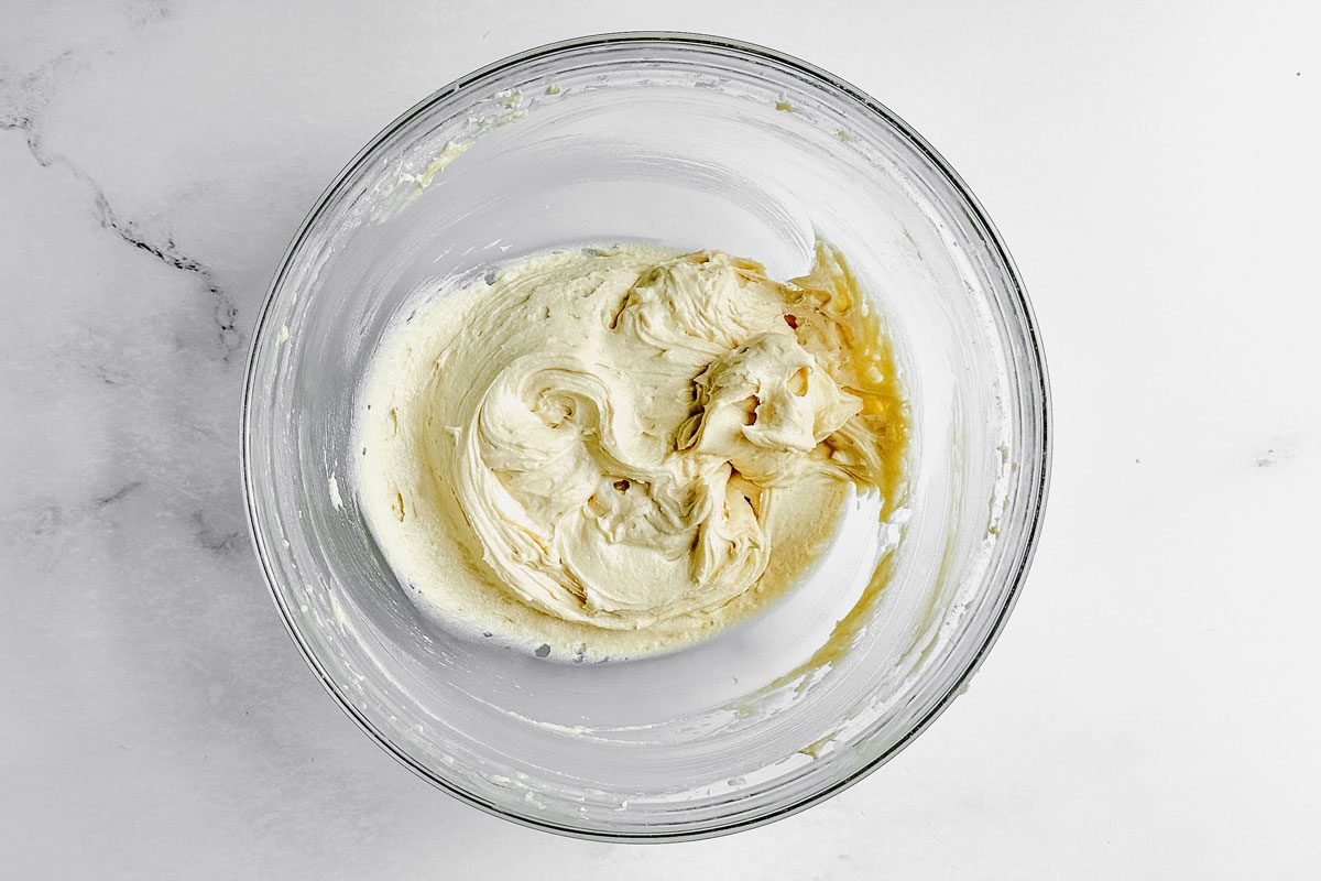 Batter for Taste of Home peach muffins in a glass bowl on a marble surface.