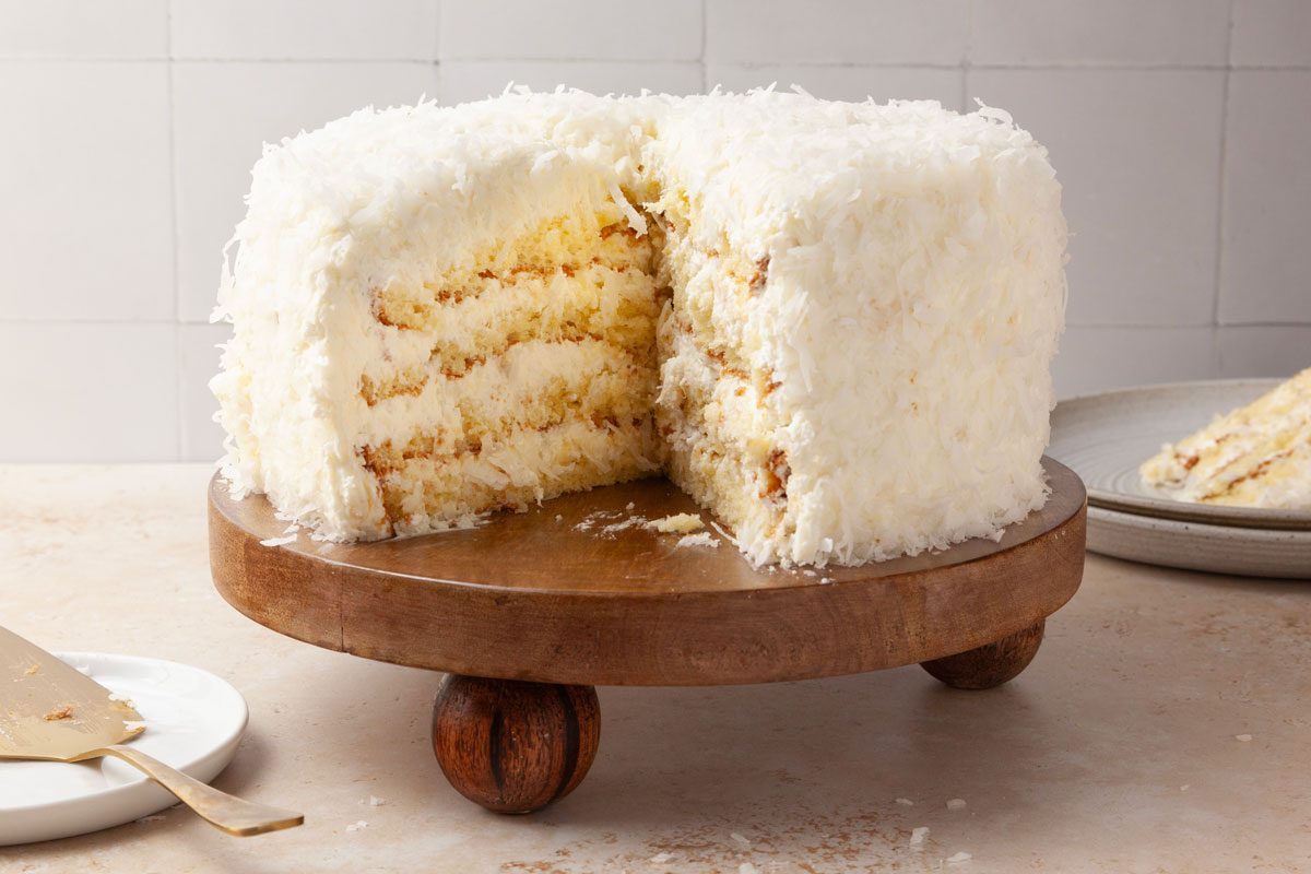 Taste of Home Pineapple Coconut Cake on a wooden platter, slices out, stack of plates