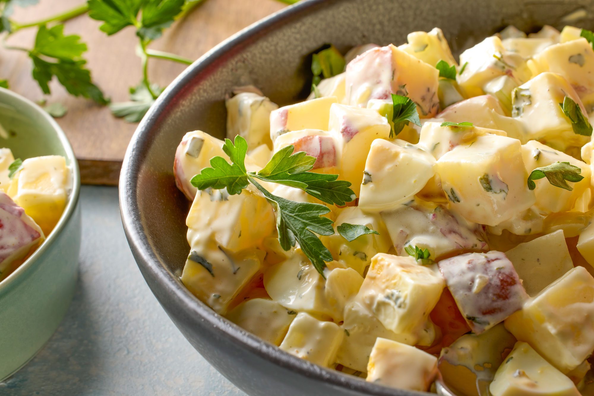 Close shot of Red Potato and Egg Salad; in a large bowl; served in bowl; wooden chopping board; celery; blue and white texture background;
