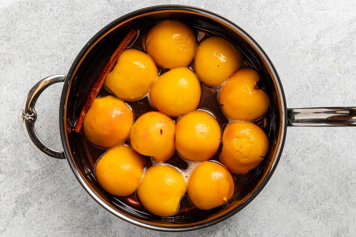 Taste of Home Spiced Peaches recipe photo of the peeled peaches poached in a saucepan.