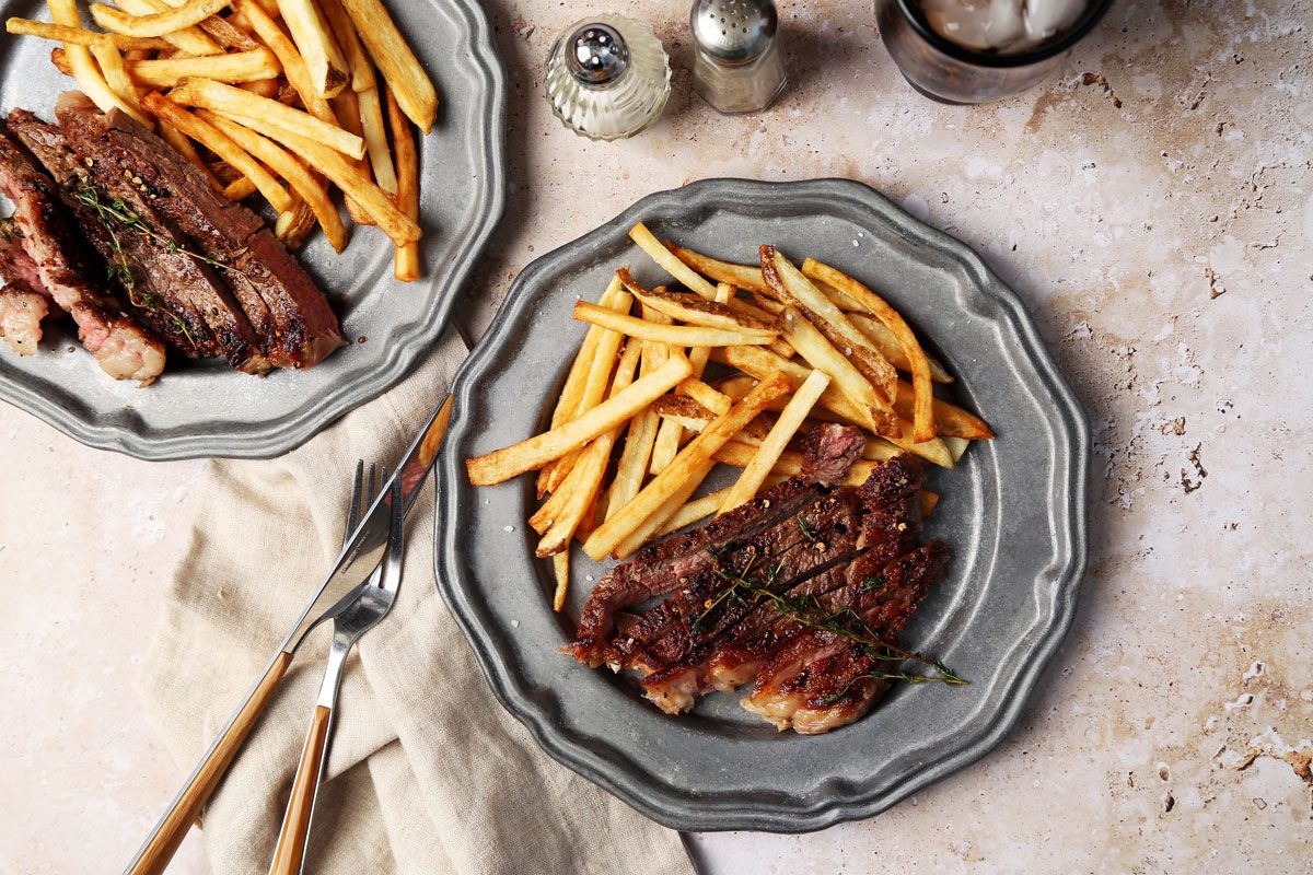 Taste of Home Steak Frites on a silver plate with a fork and knife and salt and pepper shakers.