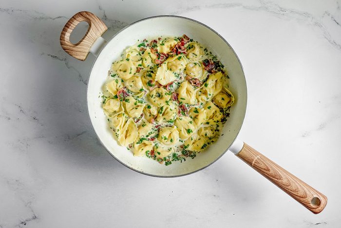 Taste of Home tortellini carbonara in a white skillet on a marble surface.