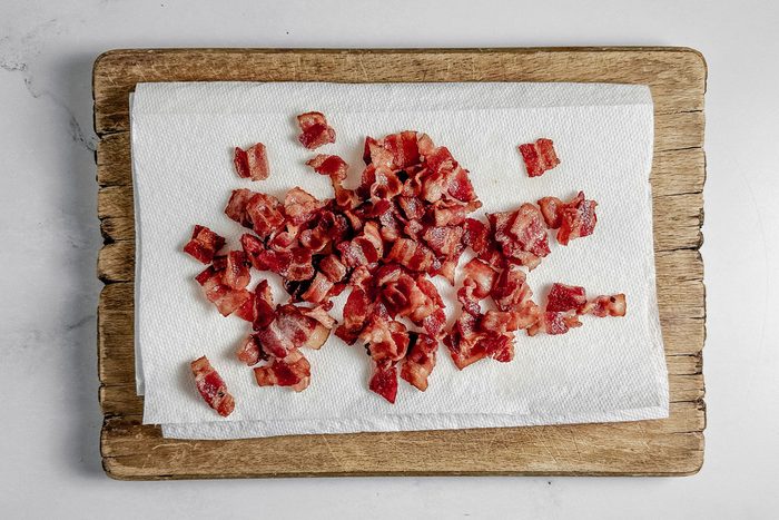 Cooked bacon on paper towels on a wooden board on a marble surface for Taste of Home tortellini carbonara.