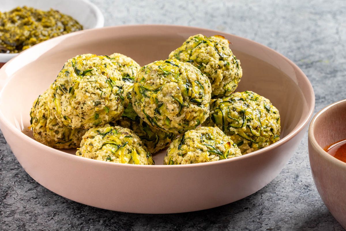 Taste of Home Zucchini Meatballs recipe photo of the finished recipe in a serving dish with pesto and marinara on the side.