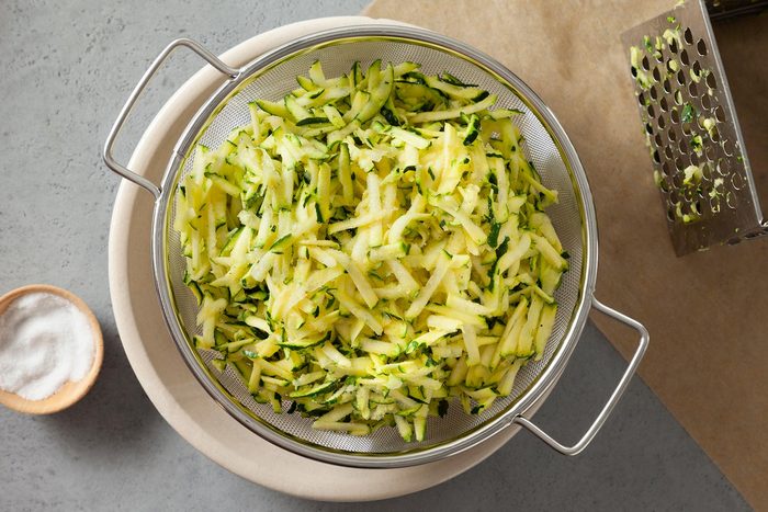 overhead shot of shredded zucchini in a strainer