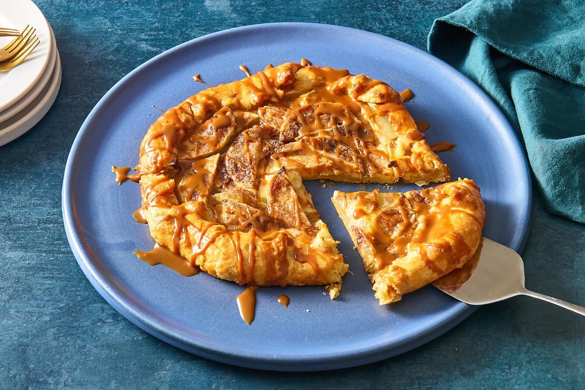 Shot of apple crostata topped with caramel sauce on a plate with a slice being removed