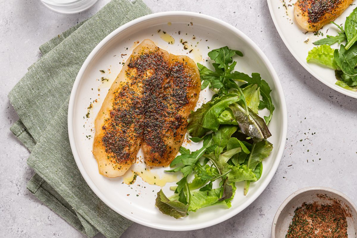 Plates With Baked Tilapia And Green Salad Leaves