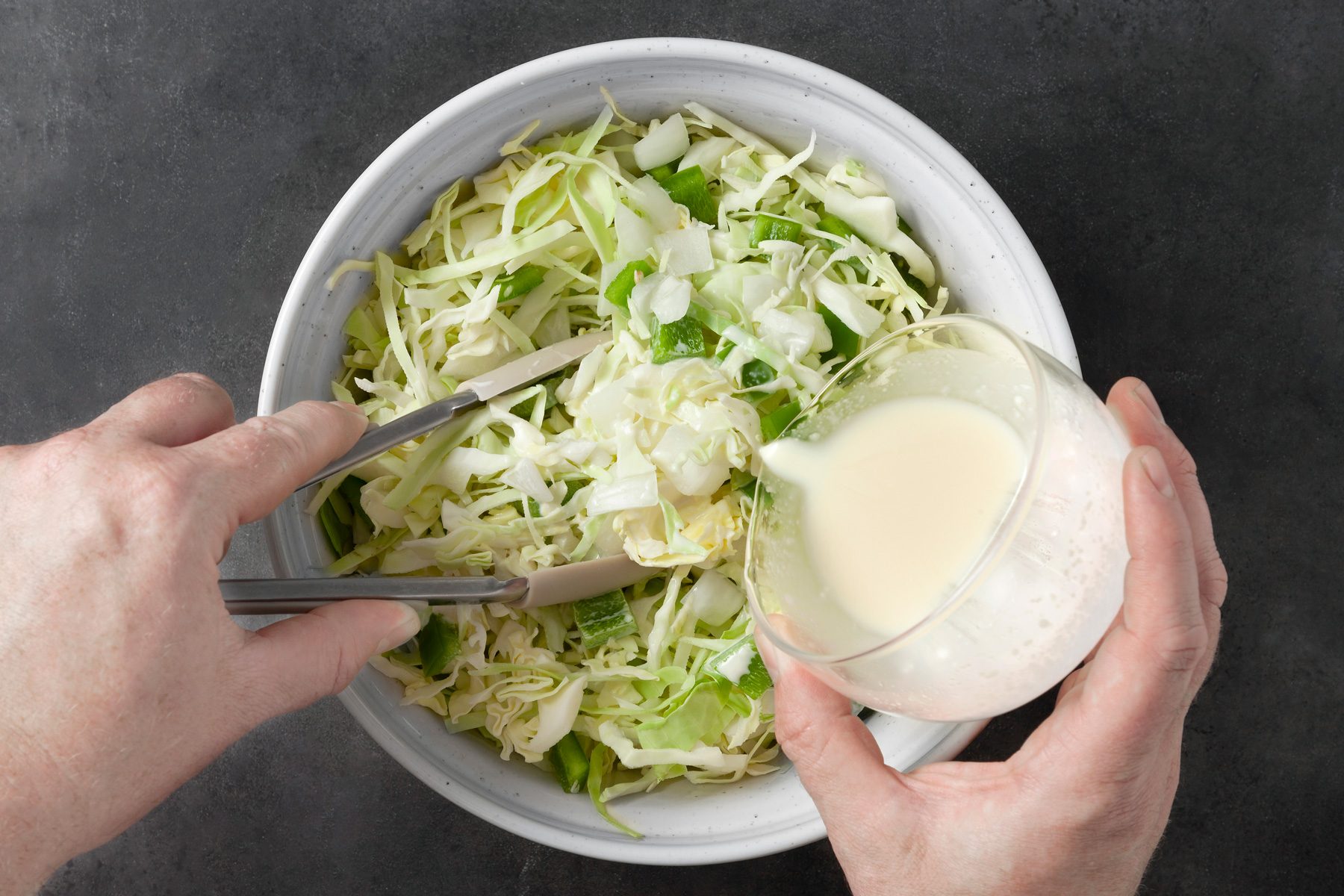 overhead shot; dark grey background; pouring cabbage mixture over salad in the bowl tossing with tong