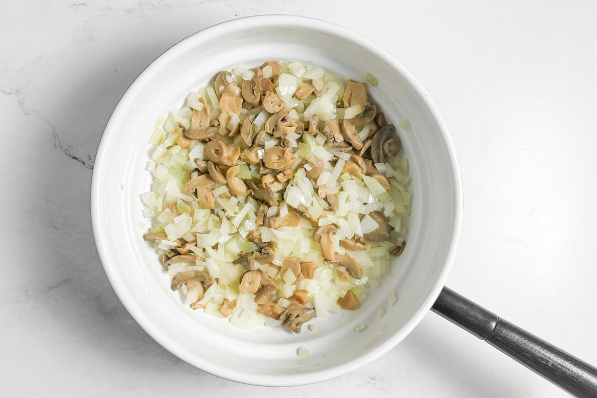 Mushrooms and onions for Taste of Home Chicken Manicotti in a white skillet