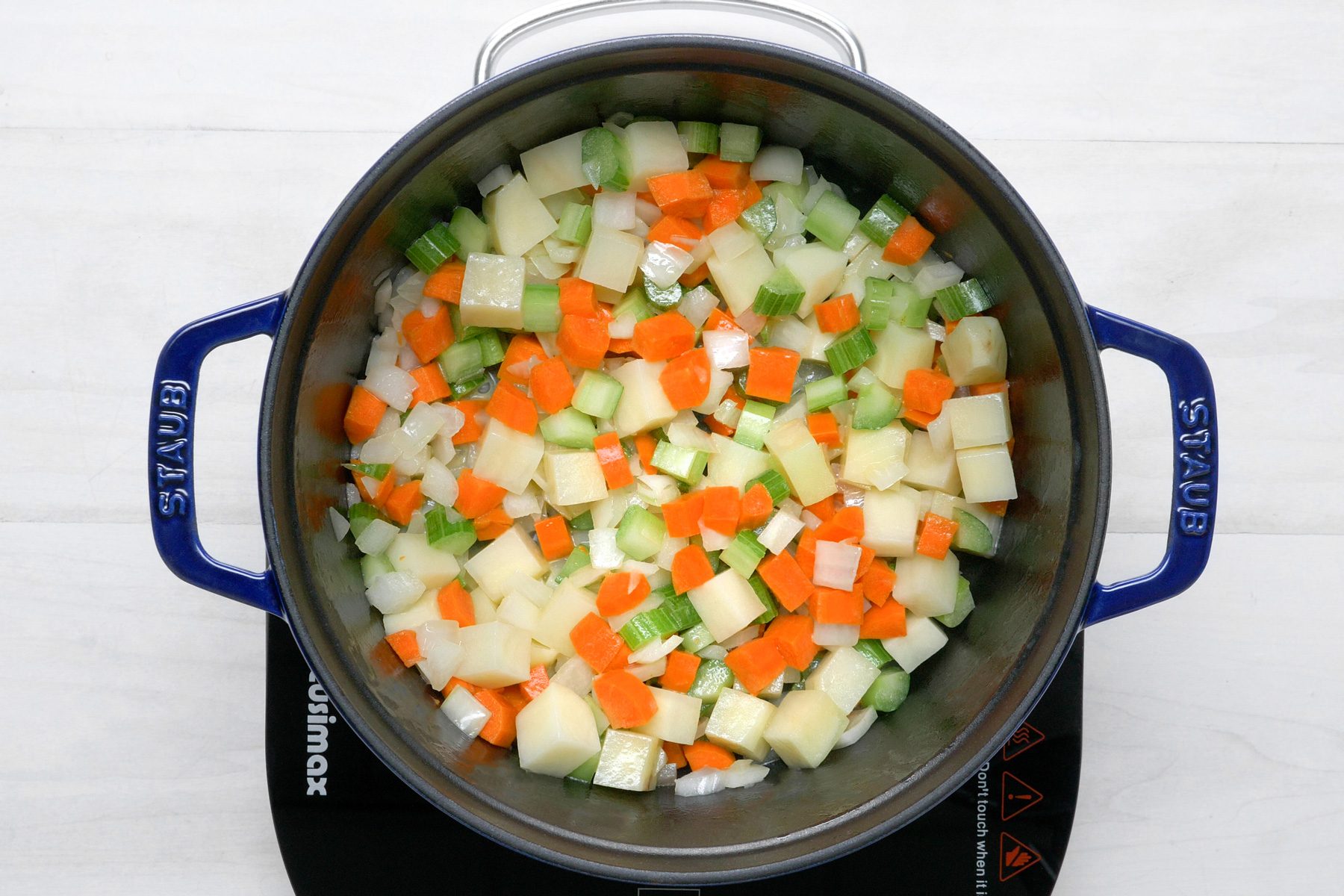 overhead shot; white wooden background; in a Dutch oven over medium-high heat, Add the potatoes, onion, celery and carrots