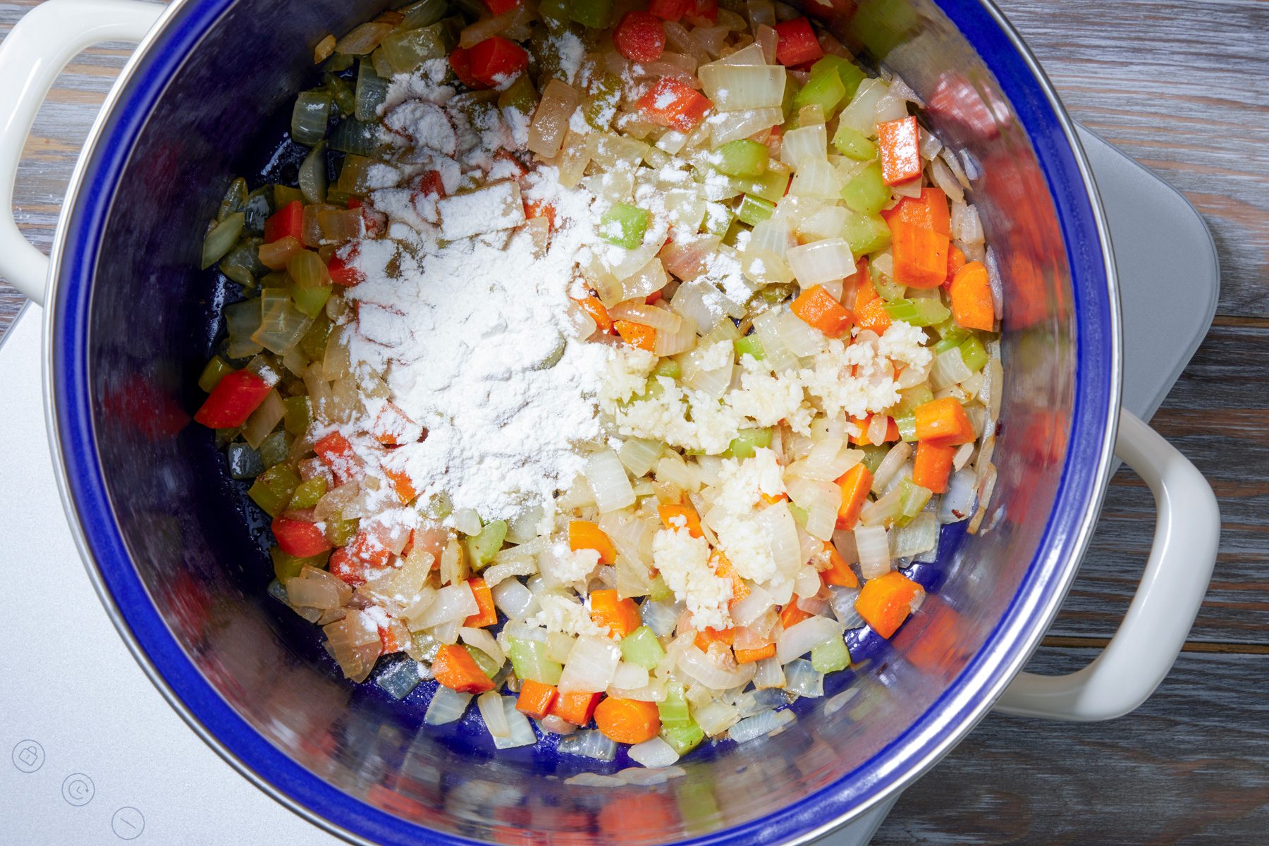 overhead shot; wooden background; added in quarter cup of flour in the pan over vegetables