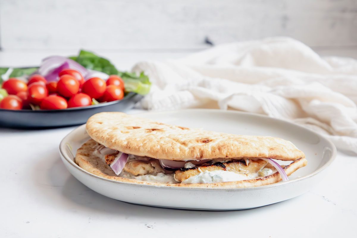 Close Up beauty shot for Taste of Home Chicken Gyros assembled on a plate with additional toppings in the background on a marble surface.