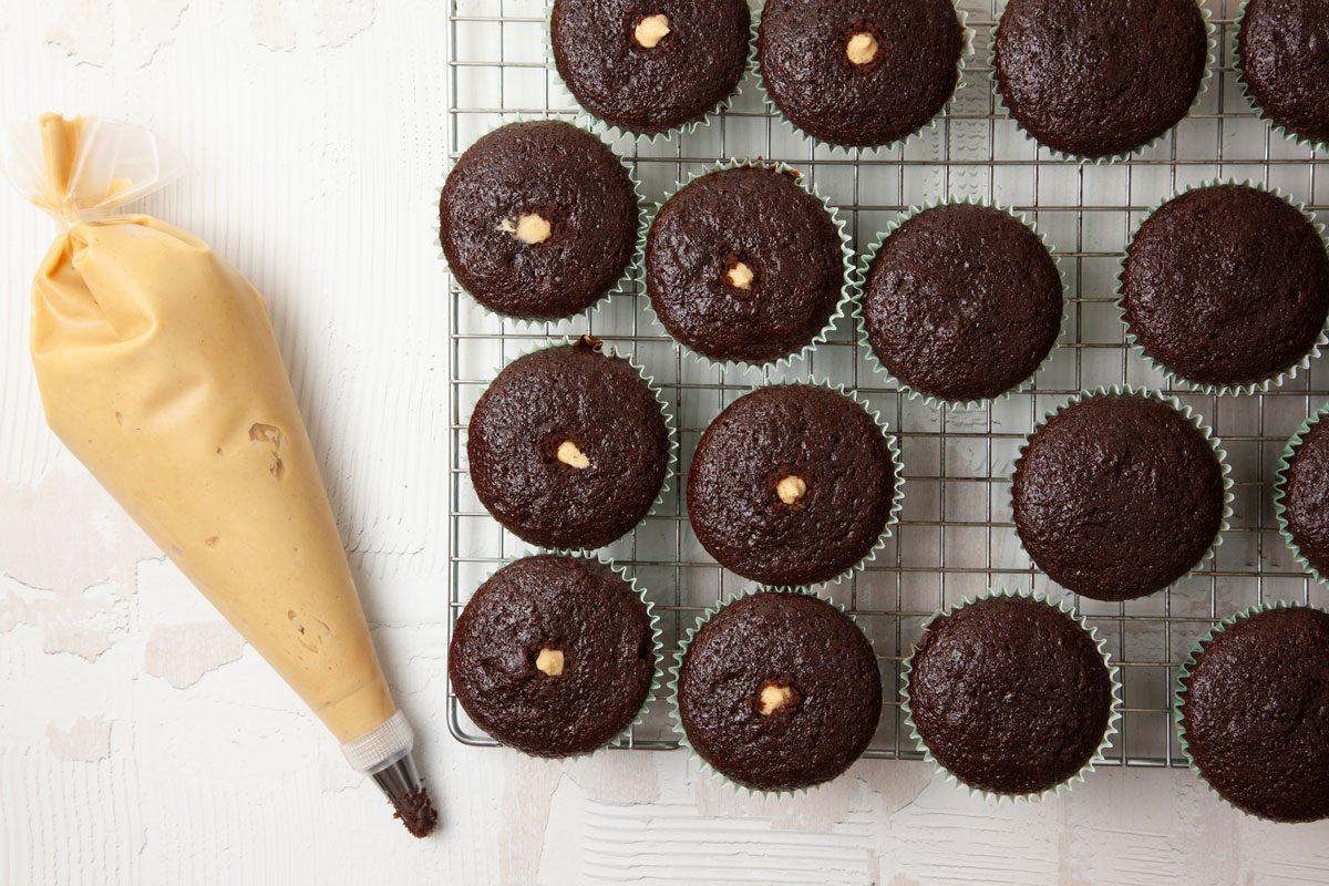 Step 3 of Taste of Home Chocolate Peanut Butter Cupcakes is to cream the peanut butter, butter, confectioners' sugar and enough milk to achieve piping consistency. Cut a small hole in the corner of a pastry bag, insert a small round tip and fill the bag with peanut butter filling. Insert the tip into the top center of each cupcake, and pipe about 1 tablespoon of filling into each.