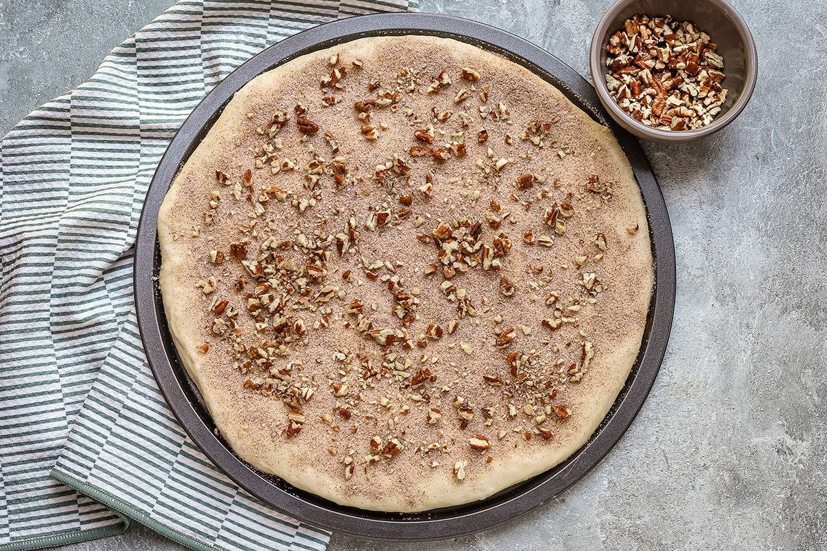 Cinnamon roll focaccia, in the pan with cinnamon sugar and pecan topping, ready to bake.