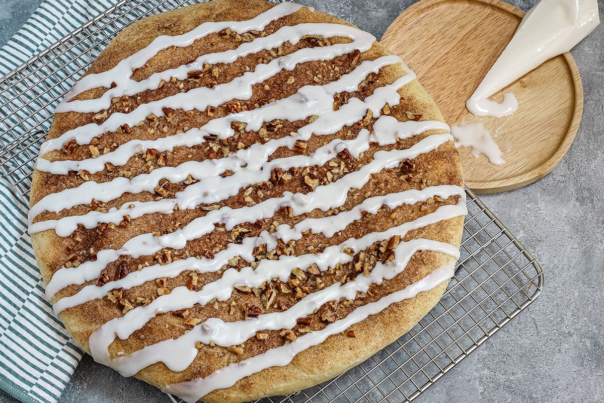 Glazed cinnamon roll focaccia with piping bag next to it.