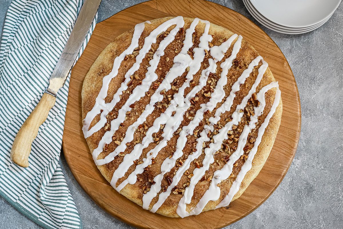 Glazed cinnamon roll focaccia with plates and knife.