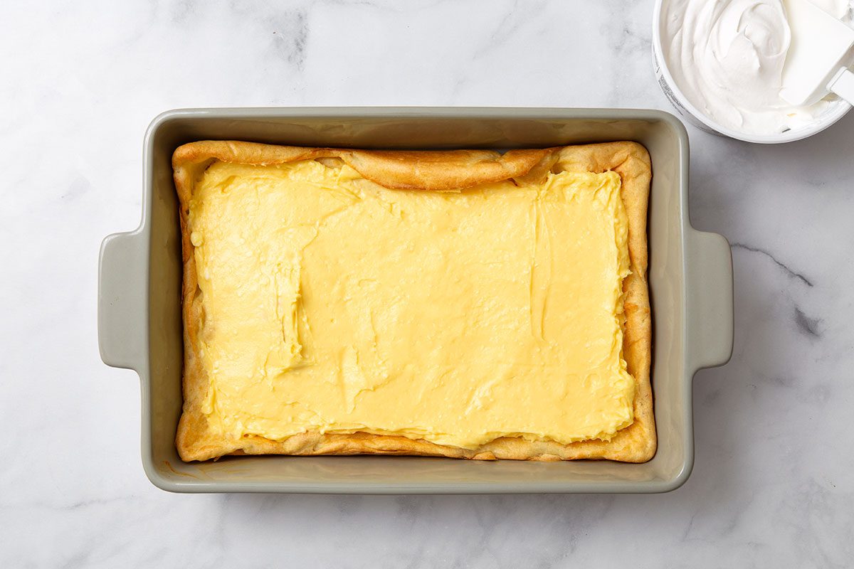 Pudding filling layered on top of pastry cake in a baking dish for step three of Cream Puff Cake recipe for Taste of Home