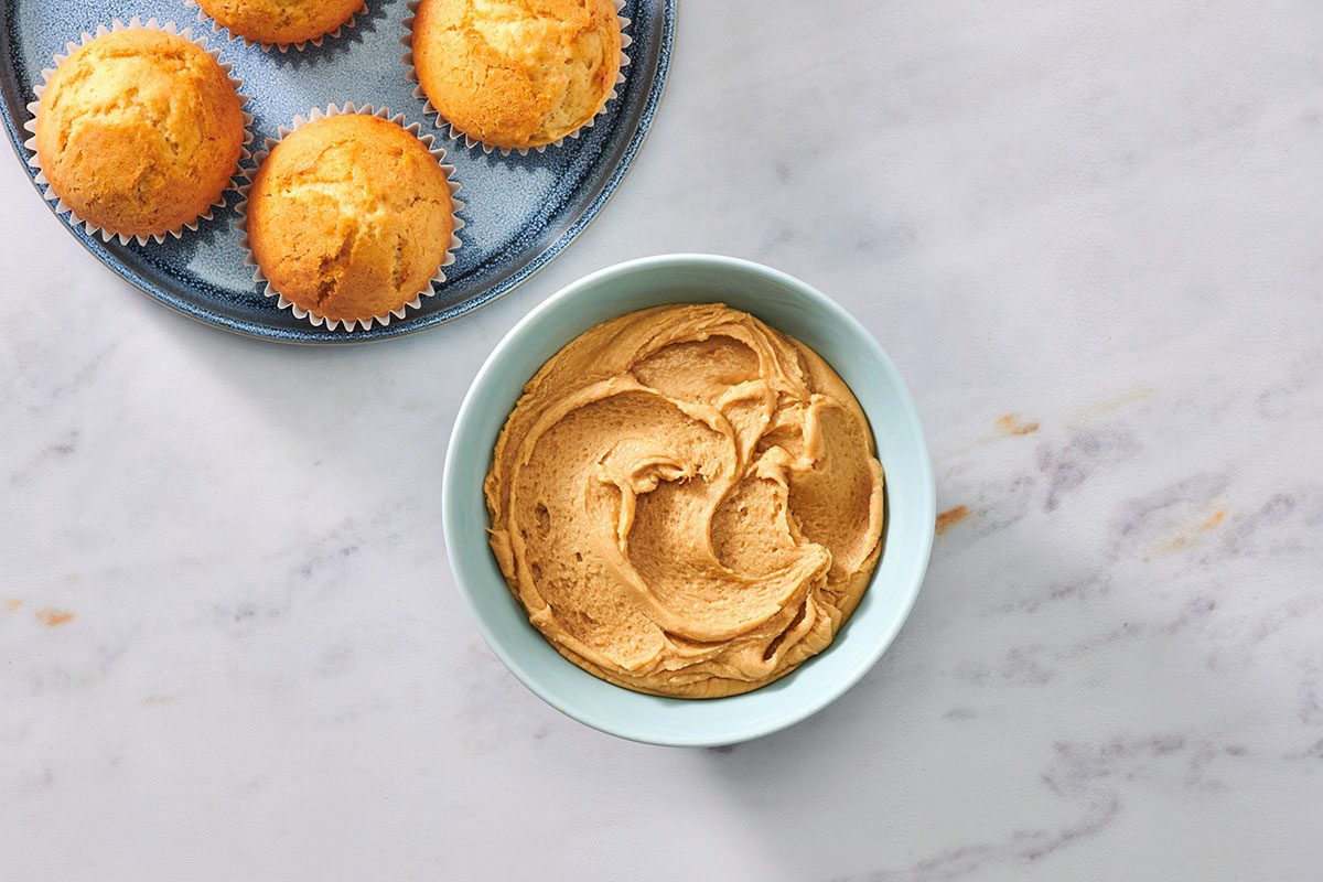 Caramel vanilla frosting spread on a muffin, with a bowl of frosting nearby