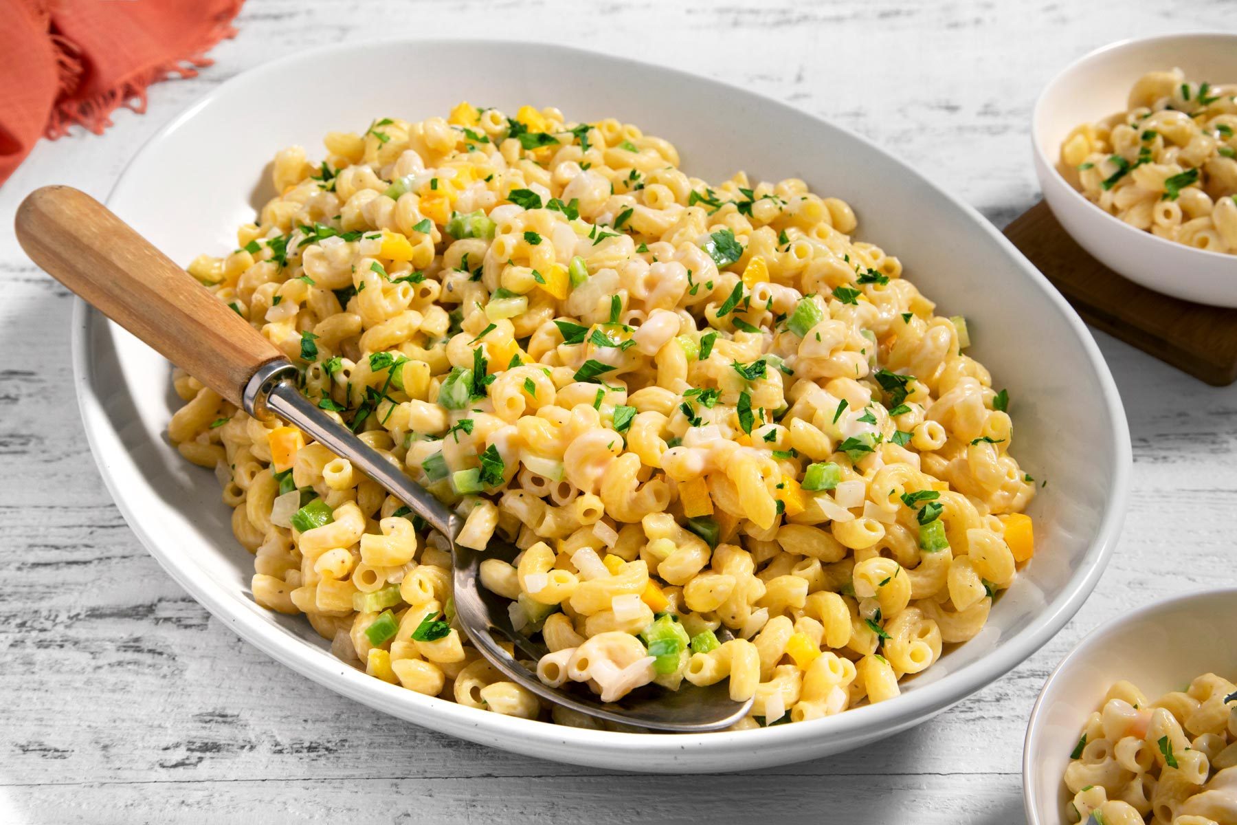3/4th shot; wooden textured background; Creamy Macaroni Salad in a oval plate with spoon; Creamy Macaroni Salad served in two small bowl