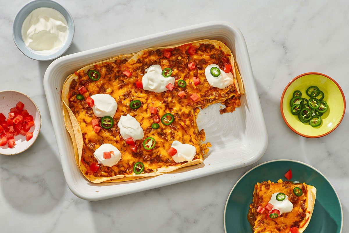 Cooked enchilada casserole with a portion removed and toppings on top 
