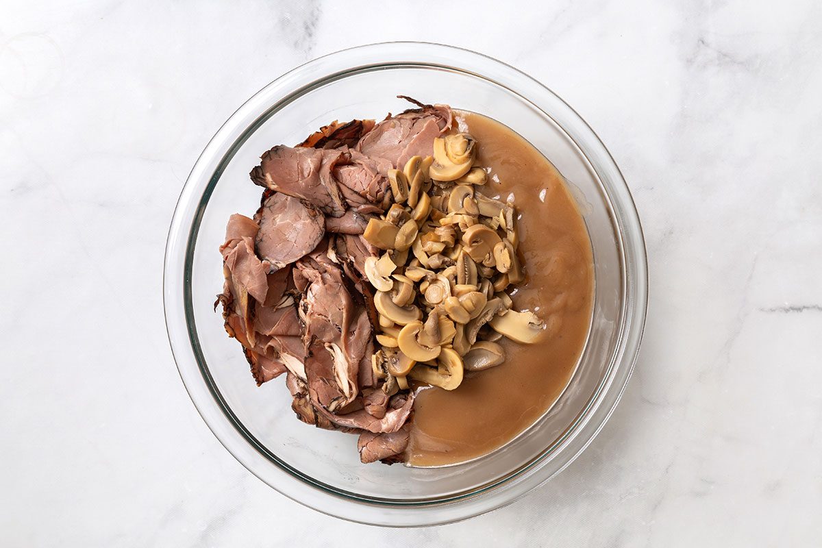 Sliced deli roast beef, beef gravy, sliced mushrooms in a mixing bowl for step one of Hot Roast Beef Sandwich Recipe for Taste of Home