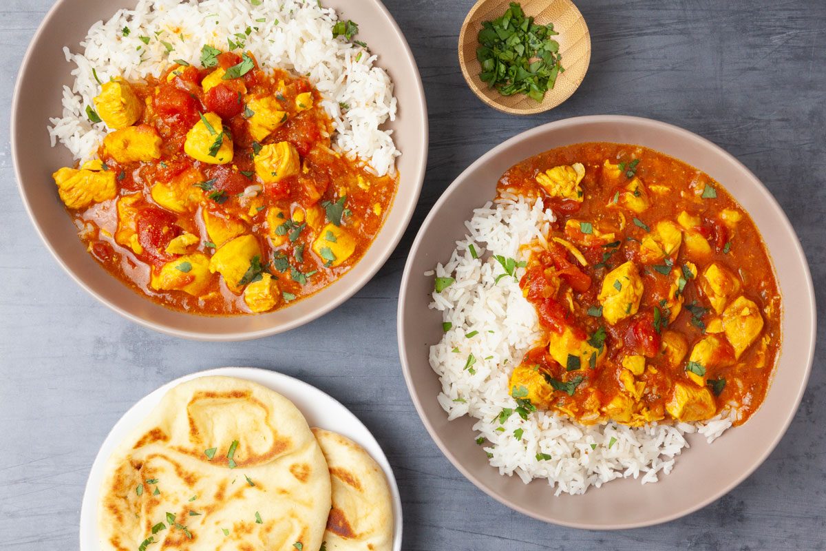 Two single servings of Taste of Home Instant Pot Chicken Curry served with rice and naan, garnished with cilantro