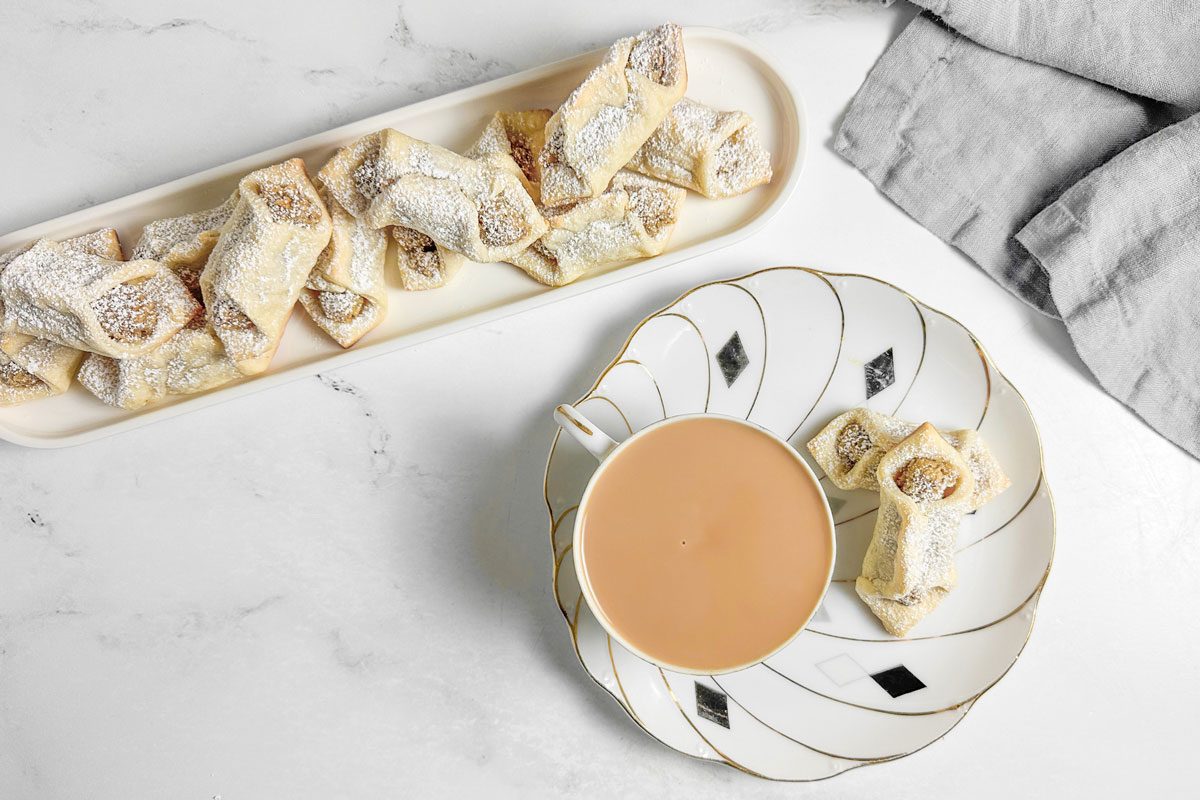 Taste of Home Kolacky Cookies on a white tray next to a cup of tea on a marble surface