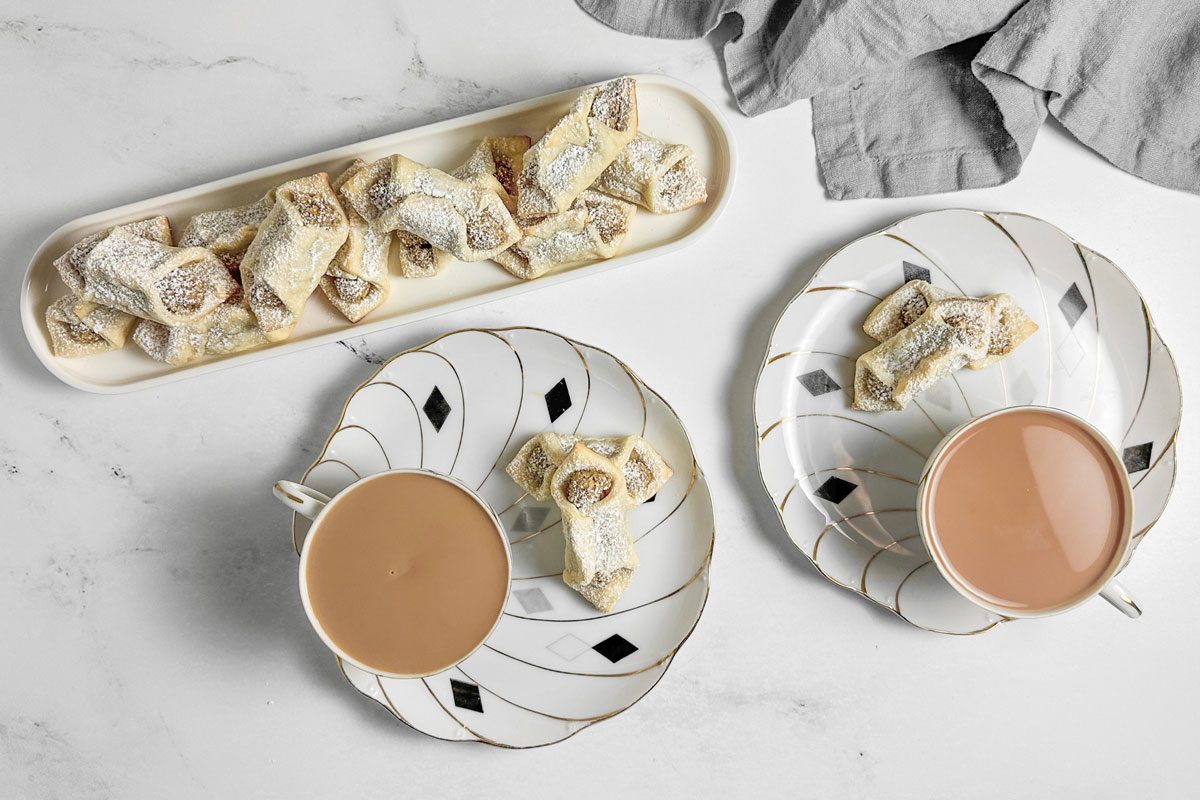 Taste of Home Kolacky Cookies on a white tray next to cups of tea on a marble surface