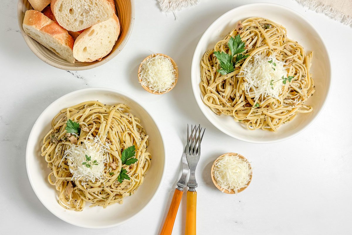 Taste of Home Linguine with Clam Sauce in white ceramic bowls next to dishes of parmesan and a bowl of bread