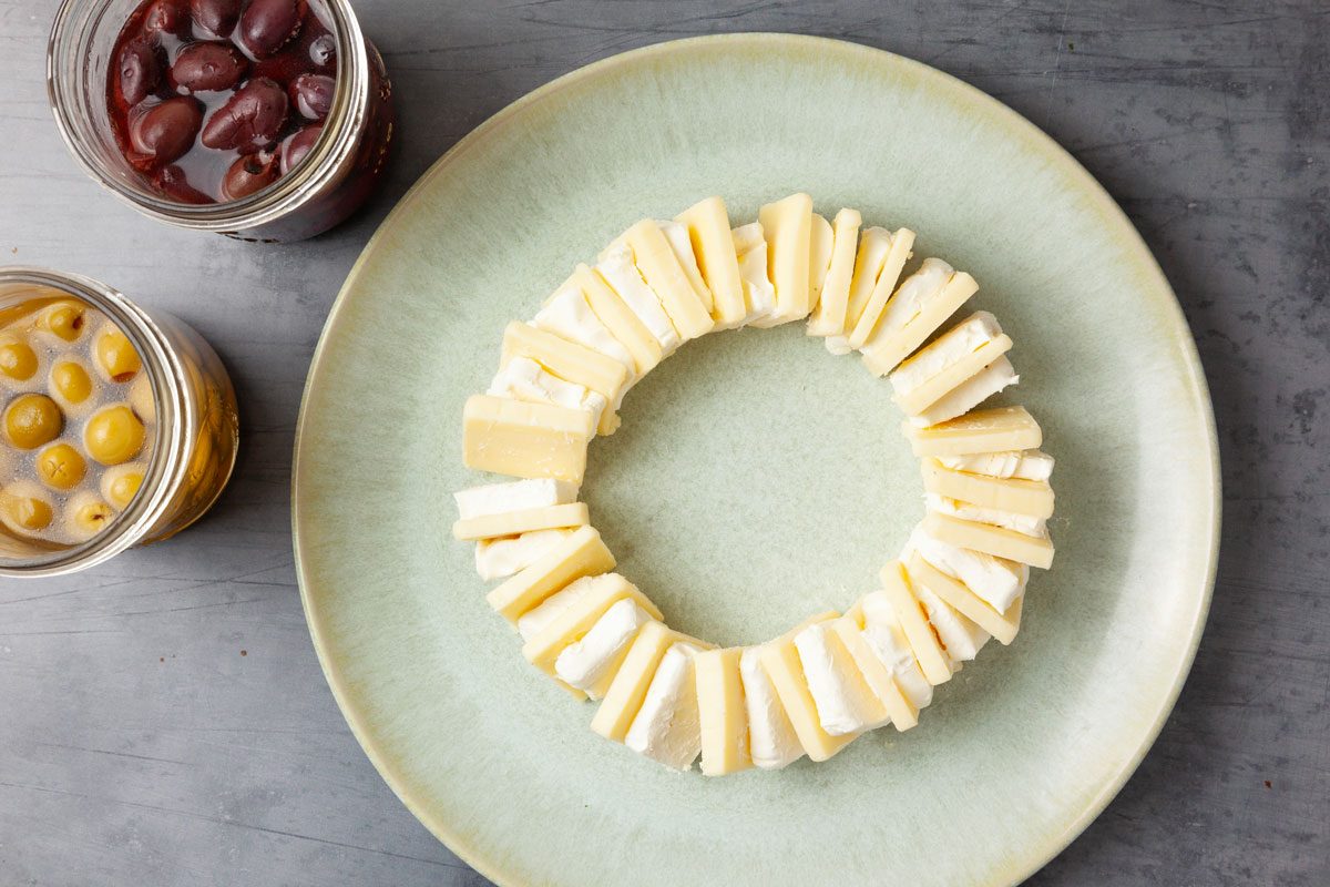 Step 1 of Taste of Home Olives & Cheese is to cut the cream cheese in half lengthwise, then cut each half into 1/4-inch slices. On a serving plate, arrange the cream cheese and the 1/4-inch slices of cheddar upright in a ring, alternating the two. Place the olives in the center.