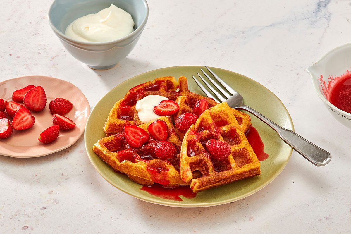 Buttermilk waffles on a plate served with whipped cream fresh strawberries and strawberry syrup