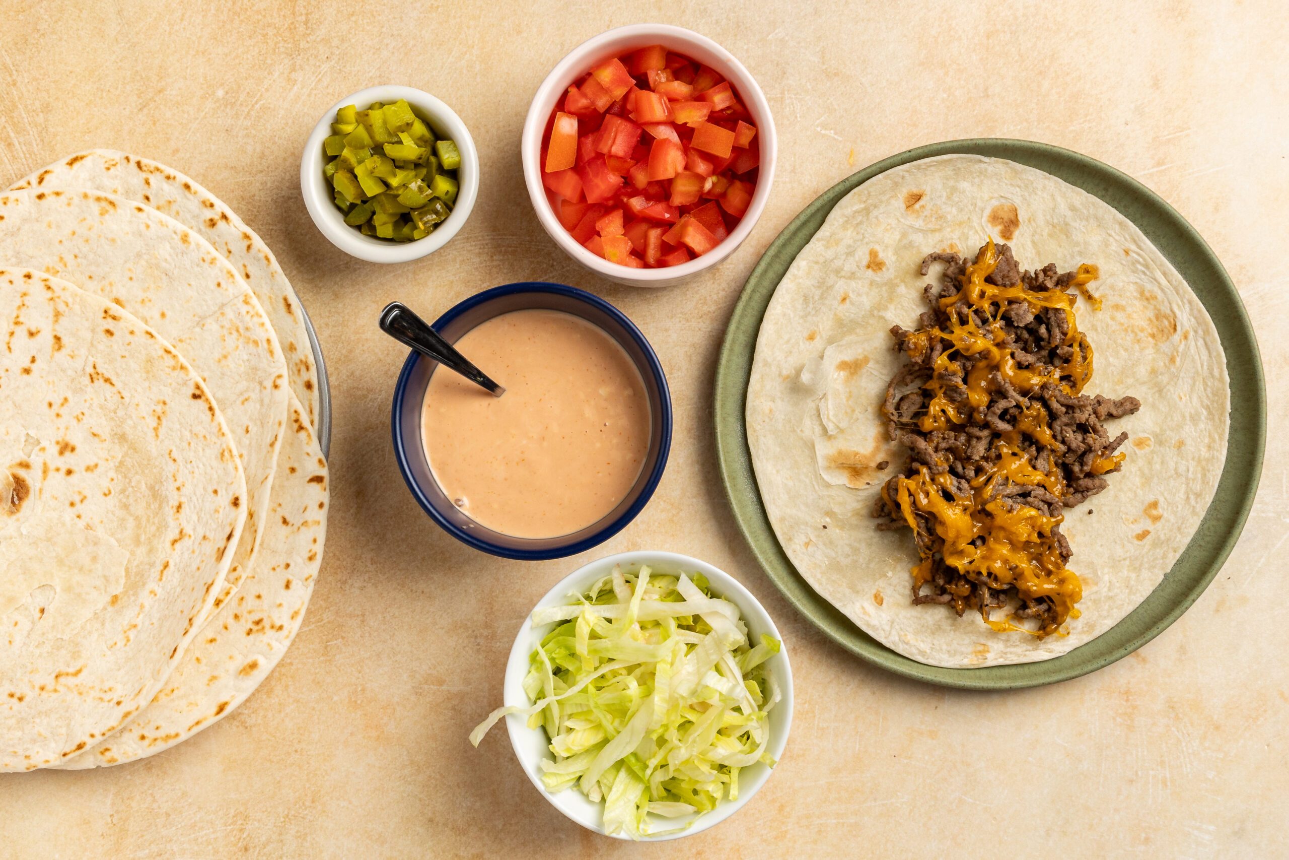 Taste of Home Cheeseburger Tacos recipe photo of the cheesy beef transferred to a tortilla with the tomato, pickles, and lettuce on side for dressing up the taco.