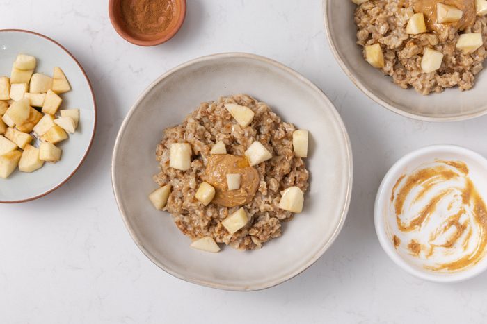Oatmeal being garnished with peanut butter and chopped apples.