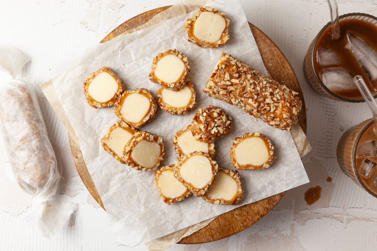 Full yield of Taste of Home Pecan Logs cut into slices on a round wooden cutting board with parchment paper, iced coffee