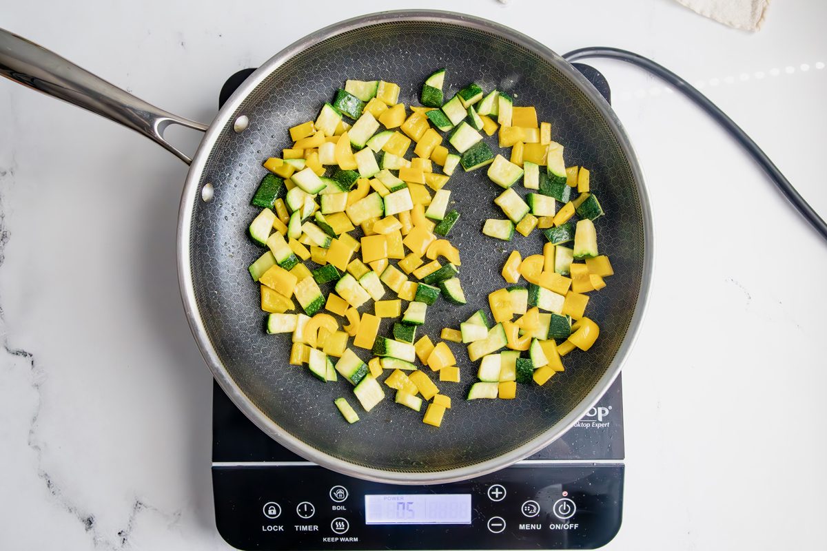 Peppers and zucchini cooking in a skillet on an induction cooktop for Taste of Home Pesto Gnocchi on a marble surface.
